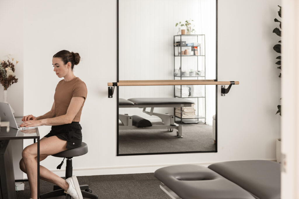 Physio typing on laptop in consultation room at dance physiotherapy clinic on the Gold Coast.
